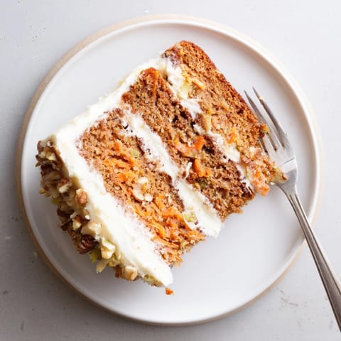 Frosted Carrot Cake slice reveals moist layers with pineapple and raisins, paired with a glass of milk on the table.