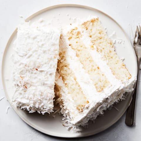 Slices of fluffy Coconut Cake reveal luscious coconut filling, paired with iced tea on a sunny brunch table.