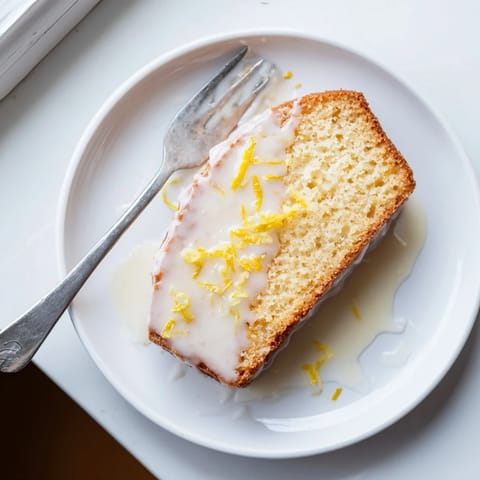 Freshly baked Lemon Pound Cake drizzled with tangy lemon glaze, served beside steaming black coffee for breakfast.