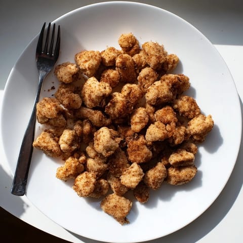 Freshly fried Popcorn Chicken nuggets showing juicy interiors and seasoned breading, arranged on a paper-lined basket alongside barbecue sauce for a delicious snack.