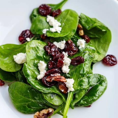 This vibrant Spinach Goat Cheese Salad is served on a white plate, featuring glossy candied pecans and ruby-red cranberries mingling with fresh spinach and soft goat cheese crumbles for a beautiful appetizer.