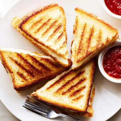 A close-up of a Mozzarella Stick Grilled Cheese sandwich oozing with gooey cheese and golden, buttery bread crust.