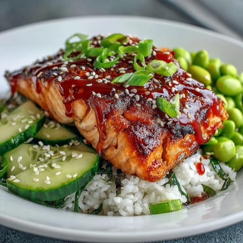 Pan-fried salmon fillets glazed in a sweet and spicy honey sriracha sauce over fluffy jasmine rice, garnished with cucumber, avocado, and edamame.