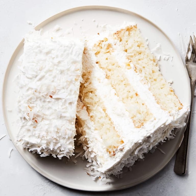 Slices of fluffy Coconut Cake reveal luscious coconut filling, paired with iced tea on a sunny brunch table.