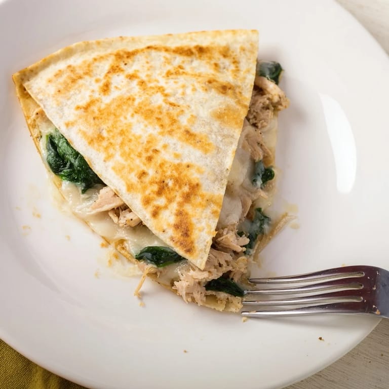 A freshly cut Chicken and Spinach Quesadilla reveals gooey mozzarella and savory filling, perfect for dipping into cool sour cream.