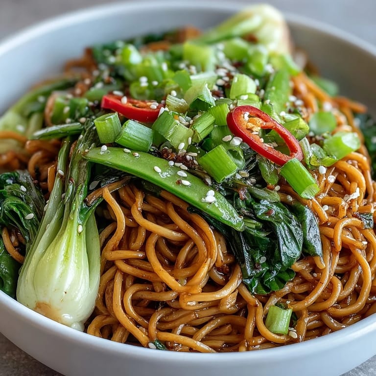 Aromatic ginger and scallion noodles with sautéed greens, garnished with sesame seeds for nutty flavor and crunch.